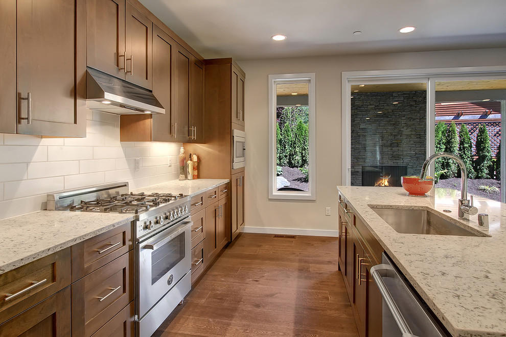 Example of a large transitional l-shaped dark wood floor open concept kitchen design in Seattle with a drop-in sink, shaker cabinets, dark wood cabinets, quartz countertops, white backsplash, ceramic backsplash, stainless steel appliances and an island