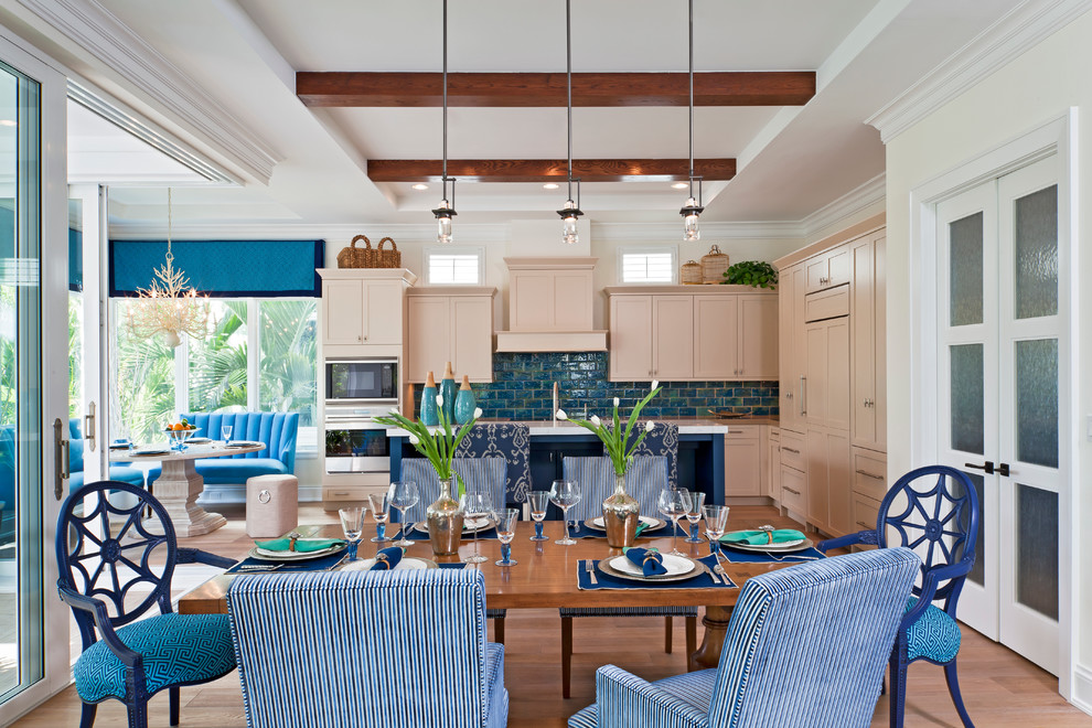 This is an example of a tropical l-shaped eat-in kitchen in Miami with recessed-panel cabinets, beige cabinets, blue splashback, stainless steel appliances, an undermount sink, quartzite benchtops, subway tile splashback, light hardwood floors and with island.
