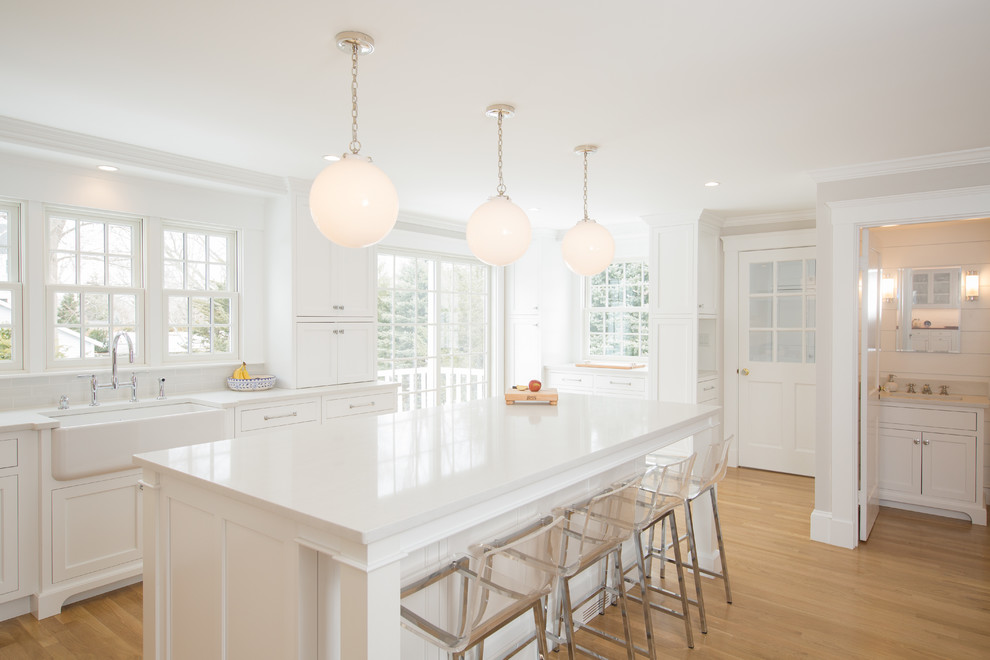 Inspiration for a mid-sized transitional l-shaped open plan kitchen in Boston with a farmhouse sink, shaker cabinets, white cabinets, quartz benchtops, white splashback, subway tile splashback, panelled appliances, medium hardwood floors, with island, white benchtop and brown floor.