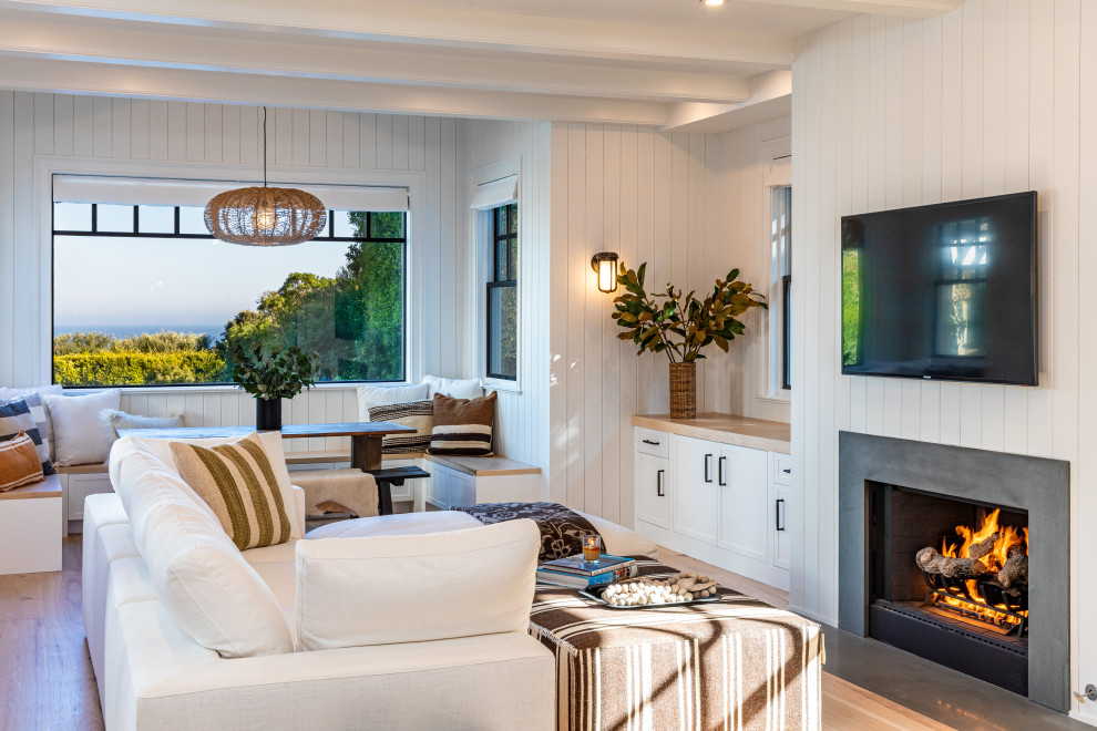 This is an example of a large beach style open concept family room in Los Angeles with white walls, light hardwood floors, a standard fireplace, a concrete fireplace surround, a wall-mounted tv, brown floor, exposed beam and panelled walls.