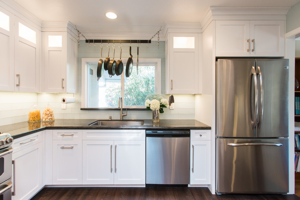 Photo of a mid-sized transitional eat-in kitchen in San Francisco with an undermount sink, glass-front cabinets, white cabinets, granite benchtops, blue splashback, glass tile splashback, stainless steel appliances, medium hardwood floors, a peninsula, brown floor and black benchtop.