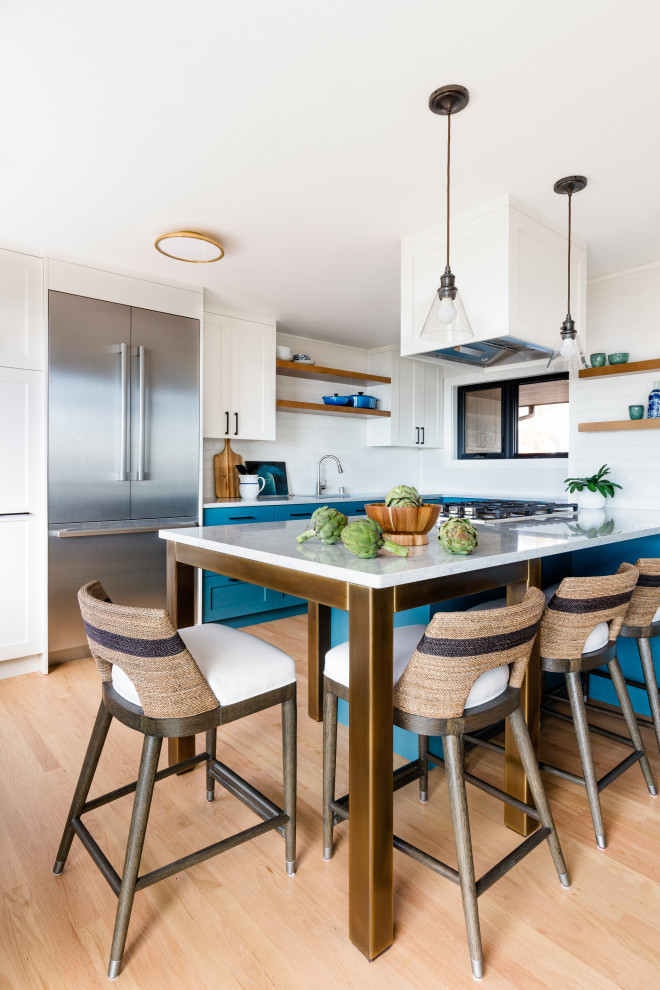 Photo of an eclectic kitchen in Seattle with an undermount sink, shaker cabinets, blue cabinets, quartz benchtops, white splashback, ceramic splashback, stainless steel appliances, light hardwood floors, a peninsula and white benchtop.