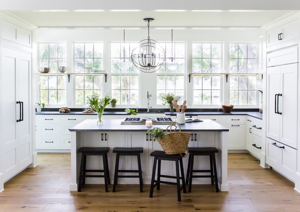 Inspiration for a coastal u-shaped medium tone wood floor and brown floor kitchen remodel in Tampa with a farmhouse sink, shaker cabinets, paneled appliances, an island and black countertops