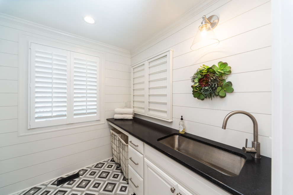Lantlig inredning av en mellanstor svarta parallell svart tvättstuga enbart för tvätt, med en undermonterad diskho, luckor med upphöjd panel, vita skåp, granitbänkskiva, vitt stänkskydd, vita väggar, marmorgolv, en tvättpelare och grått golv