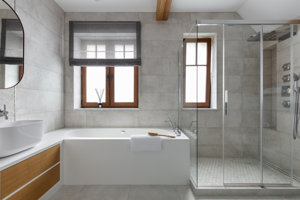 На фото: большая ванная комната в белых тонах с отделкой деревом в современном стиле с плоскими фасадами, светлыми деревянными фасадами, полновстраиваемой ванной, открытым душем, инсталляцией, серой плиткой, керамогранитной плиткой, серыми стенами, полом из керамогранита, душевой кабиной, настольной раковиной, столешницей из искусственного камня, серым полом, душем с раздвижными дверями, белой столешницей, окном, тумбой под две раковины, напольной тумбой и балками на потолке с