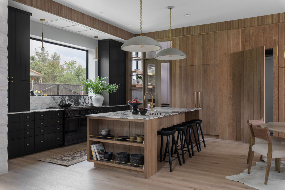 Inspiration for a transitional single-wall light wood floor eat-in kitchen remodel in Austin with an undermount sink, black cabinets, black appliances, an island and multicolored countertops