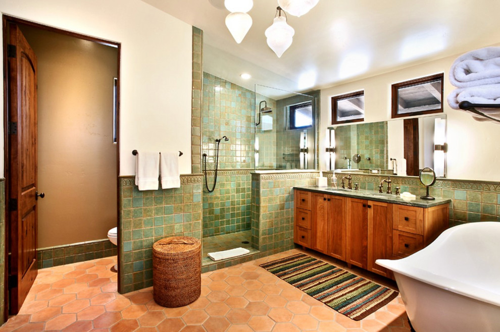 Пример оригинального дизайна: большая главная ванная комната в средиземноморском стиле с коричневыми фасадами, отдельно стоящей ванной, душем в нише, унитазом-моноблоком, зеленой плиткой, белыми стенами, накладной раковиной, оранжевым полом, открытым душем, тумбой под две раковины и встроенной тумбой