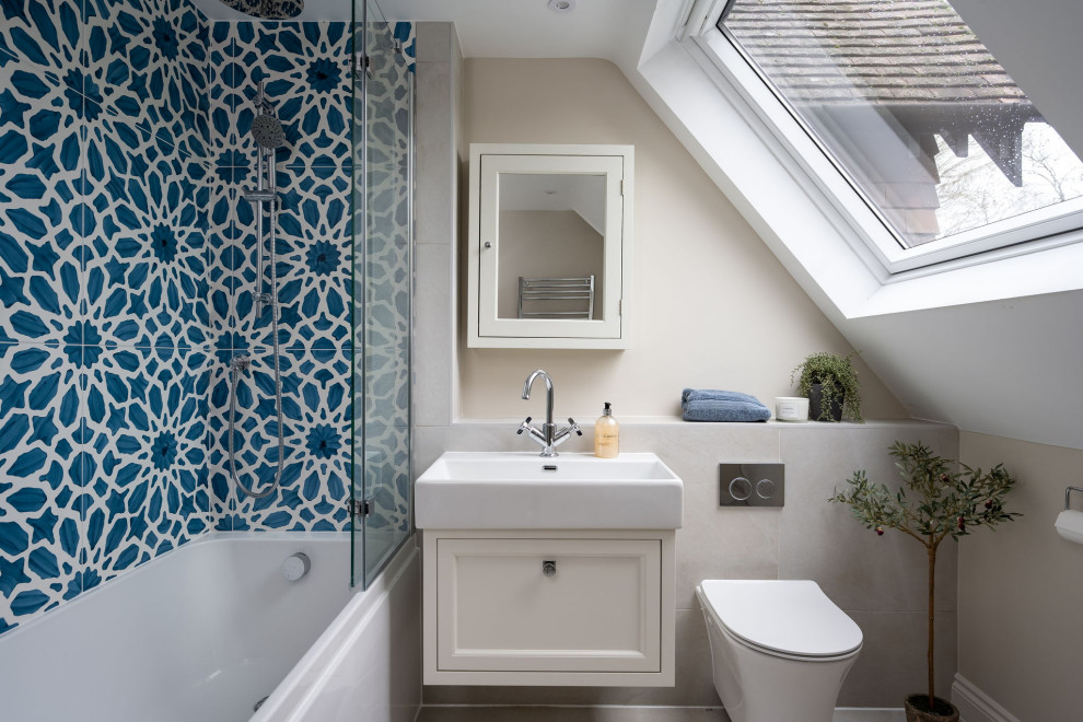 Inspiration for a medium sized traditional family bathroom in Berkshire with shaker cabinets, beige cabinets, a built-in bath, a shower/bath combination, a wall mounted toilet, blue tiles, ceramic tiles, beige walls, porcelain flooring, a built-in sink, beige floors, a hinged door, a feature wall, a single sink and a floating vanity unit.