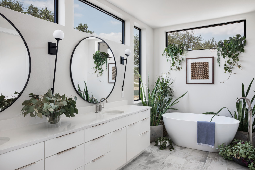 This is an example of a large contemporary master bathroom in Austin with flat-panel cabinets, white cabinets, a freestanding tub, gray tile, stone tile, white walls, ceramic floors, an undermount sink, quartzite benchtops, grey floor, a hinged shower door, white benchtops, a double vanity and a floating vanity.