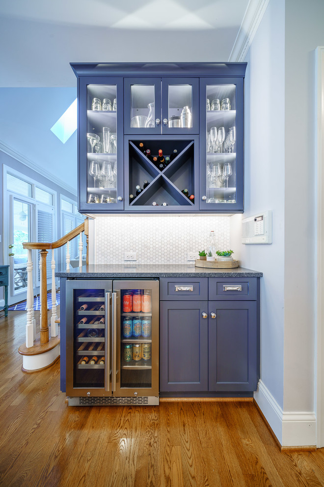 Photo of a transitional u-shaped home bar in Other with no sink, shaker cabinets, blue cabinets, white splashback, mosaic tile splashback, medium hardwood floors, brown floor and grey benchtop.