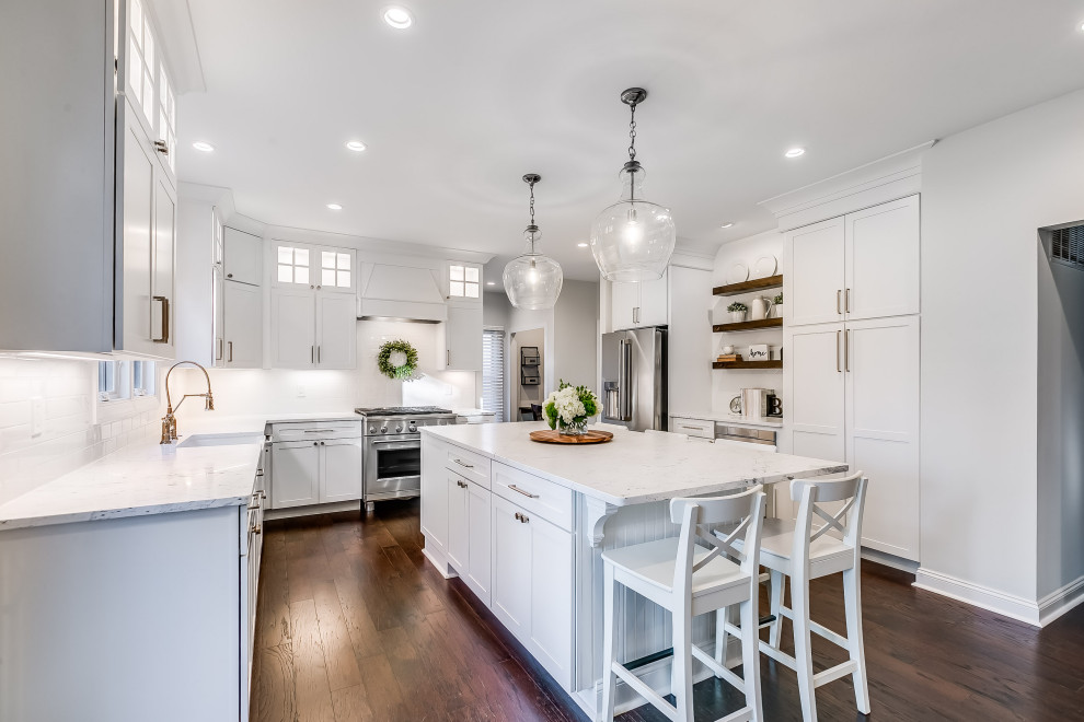 Inspiration for a mid-sized country u-shaped kitchen in Baltimore with a farmhouse sink, shaker cabinets, white cabinets, marble benchtops, white splashback, ceramic splashback, stainless steel appliances, dark hardwood floors, with island, brown floor and white benchtop.