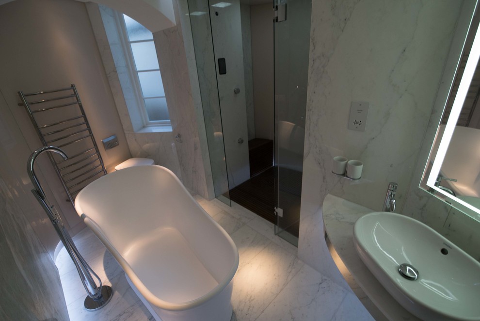 Large contemporary master bathroom in London with a freestanding tub, a wall-mount toilet, multi-coloured tile, glass sheet wall, multi-coloured walls, marble floors, a vessel sink, marble benchtops and an alcove shower.