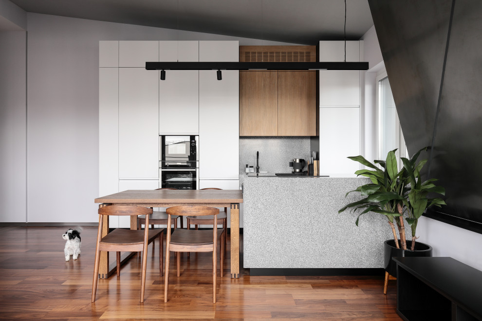 Large scandinavian galley eat-in kitchen in Saint Petersburg with a single-bowl sink, flat-panel cabinets, white cabinets, solid surface benchtops, grey splashback, engineered quartz splashback, black appliances, medium hardwood floors, with island, brown floor, grey benchtop and vaulted.