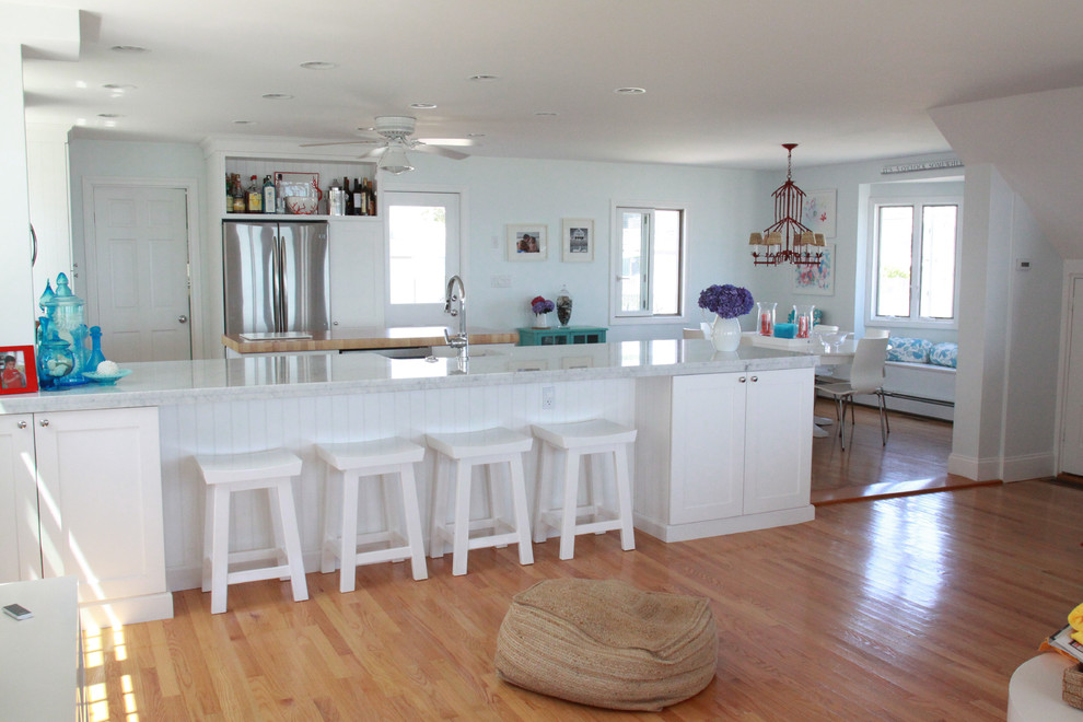 Large beach style u-shaped eat-in kitchen in Boston with a farmhouse sink, shaker cabinets, white cabinets, quartz benchtops, blue splashback, subway tile splashback, stainless steel appliances, light hardwood floors, with island and brown floor.