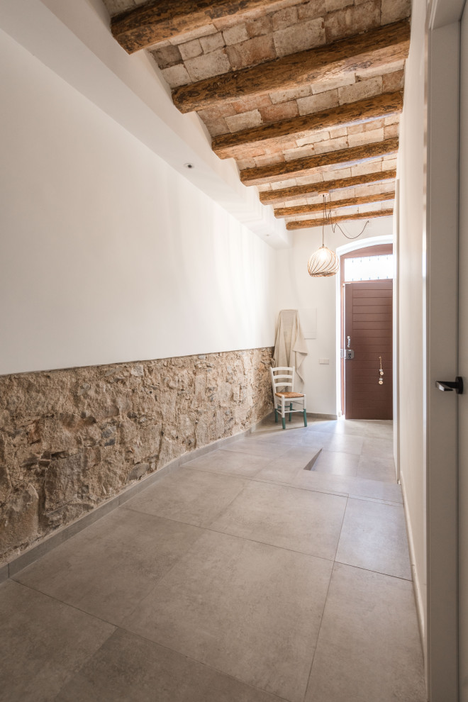Large modern vestibule in Barcelona with white walls, ceramic floors, a single front door, a dark wood front door, beige floor, exposed beam and brick walls.