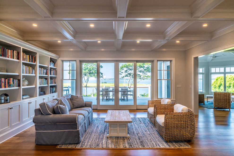 This is an example of a beach style open concept living room in New York with a library, grey walls, medium hardwood floors and brown floor.