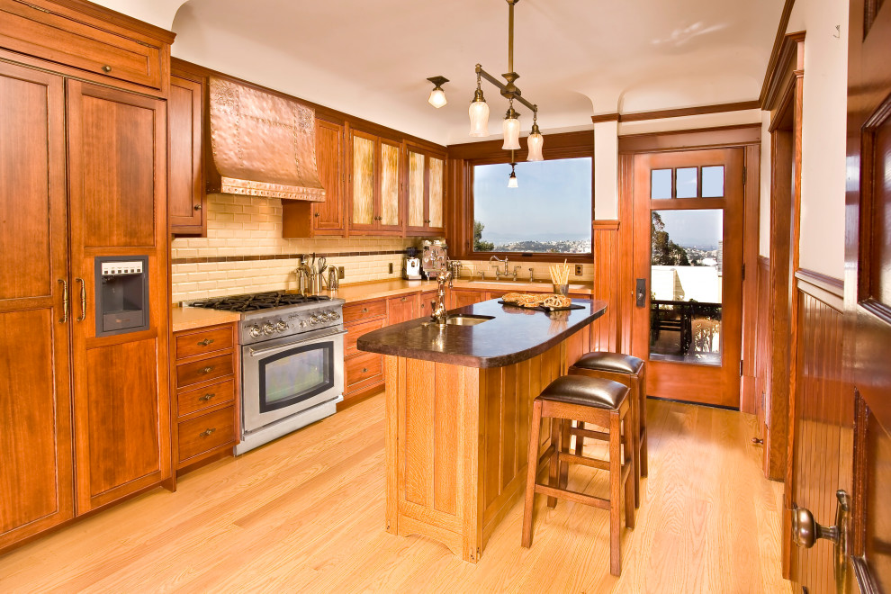 Inspiration for a mid-sized craftsman light wood floor and brown floor kitchen remodel in San Francisco with a single-bowl sink, recessed-panel cabinets, medium tone wood cabinets, quartzite countertops, yellow backsplash, ceramic backsplash, stainless steel appliances, an island and orange countertops