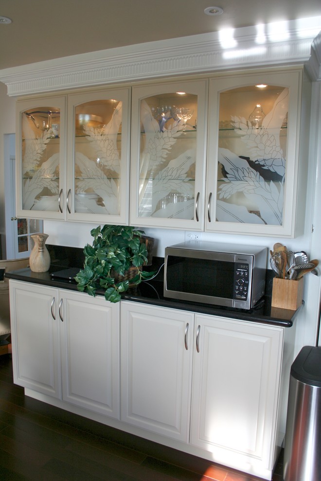 Photo of a traditional kitchen in Hawaii with white cabinets and black splashback.