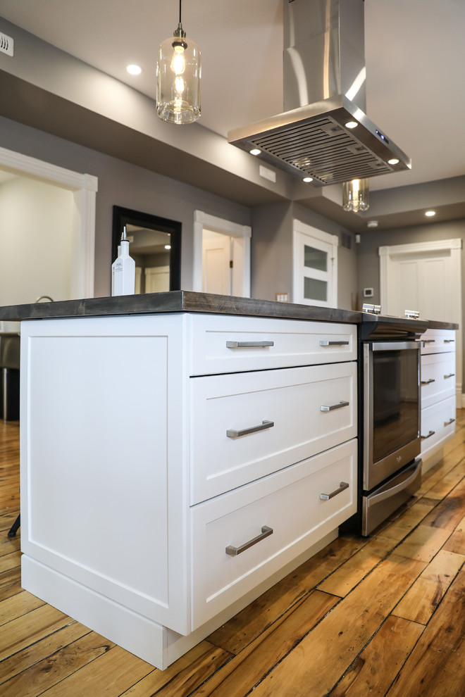 Mid-sized transitional single-wall medium tone wood floor and brown floor eat-in kitchen photo with a farmhouse sink, shaker cabinets, white cabinets, white backsplash, stainless steel appliances, an island and white countertops