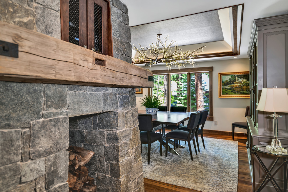 This is an example of a mid-sized country separate dining room in Other with grey walls, medium hardwood floors, a two-sided fireplace, a stone fireplace surround and brown floor.