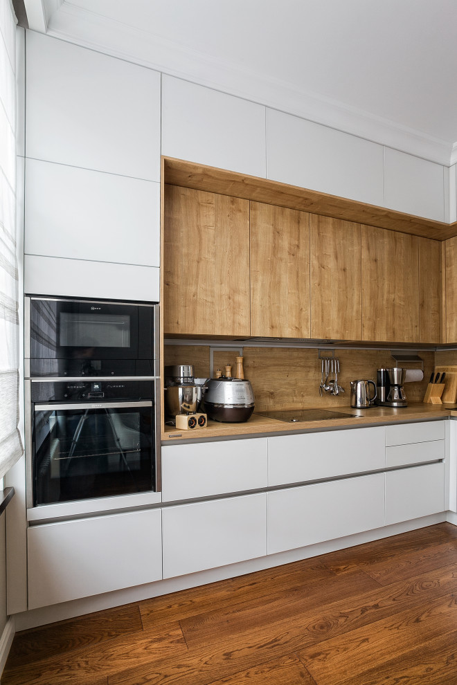 Mid-sized scandinavian l-shaped eat-in kitchen in Other with a single-bowl sink, glass-front cabinets, white cabinets, laminate benchtops, brown splashback, black appliances, painted wood floors, no island, brown floor and brown benchtop.