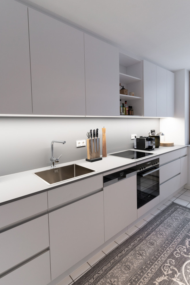 Mittelgroße Moderne Küche in L-Form mit flächenbündigen Schrankfronten, weißen Schränken, Laminat-Arbeitsplatte, Küchenrückwand in Grau und grauer Arbeitsplatte