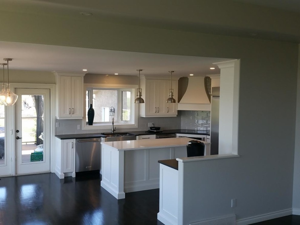 Kitchen - mid-sized transitional dark wood floor and brown floor kitchen idea with a farmhouse sink, shaker cabinets, white cabinets, quartz countertops, gray backsplash, subway tile backsplash, stainless steel appliances and an island
