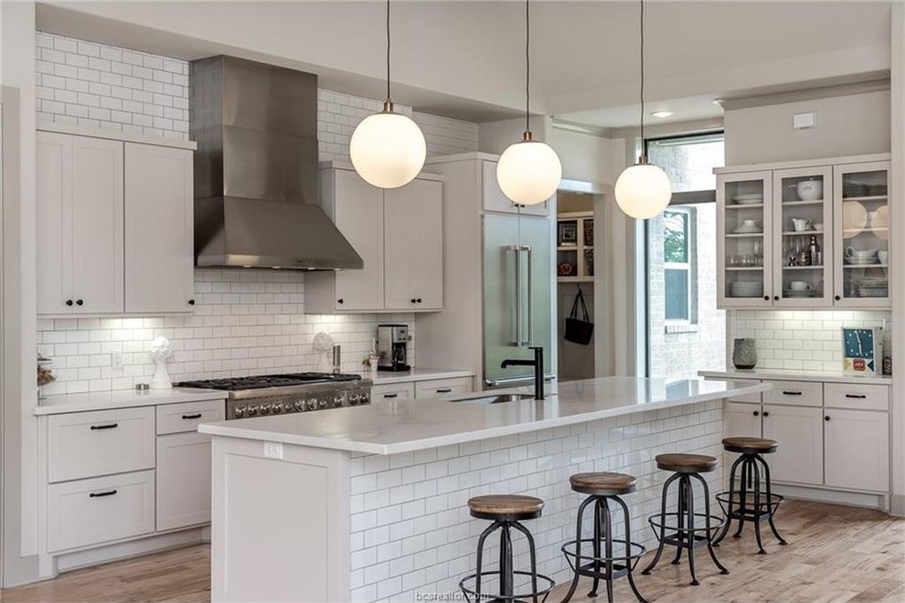 Design ideas for a large industrial single-wall open plan kitchen in Austin with an undermount sink, shaker cabinets, white cabinets, subway tile splashback, stainless steel appliances and with island.