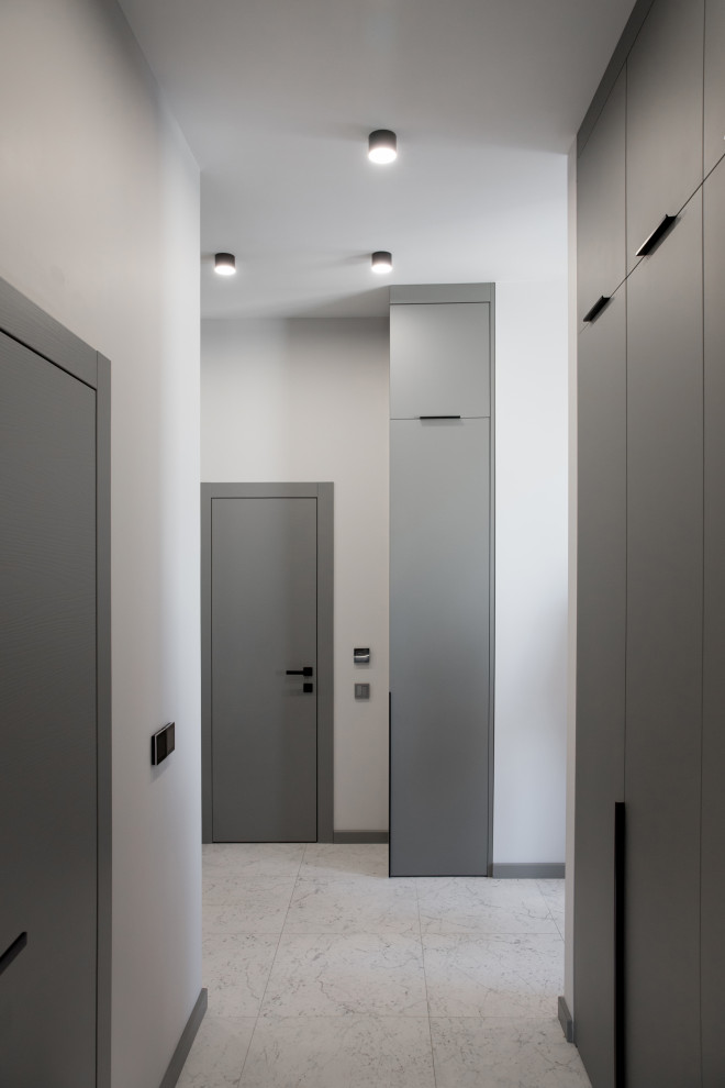 На фото: узкая прихожая среднего размера со шкафом для обуви в скандинавском стиле с серыми стенами, полом из керамогранита, одностворчатой входной дверью, серой входной дверью и белым полом