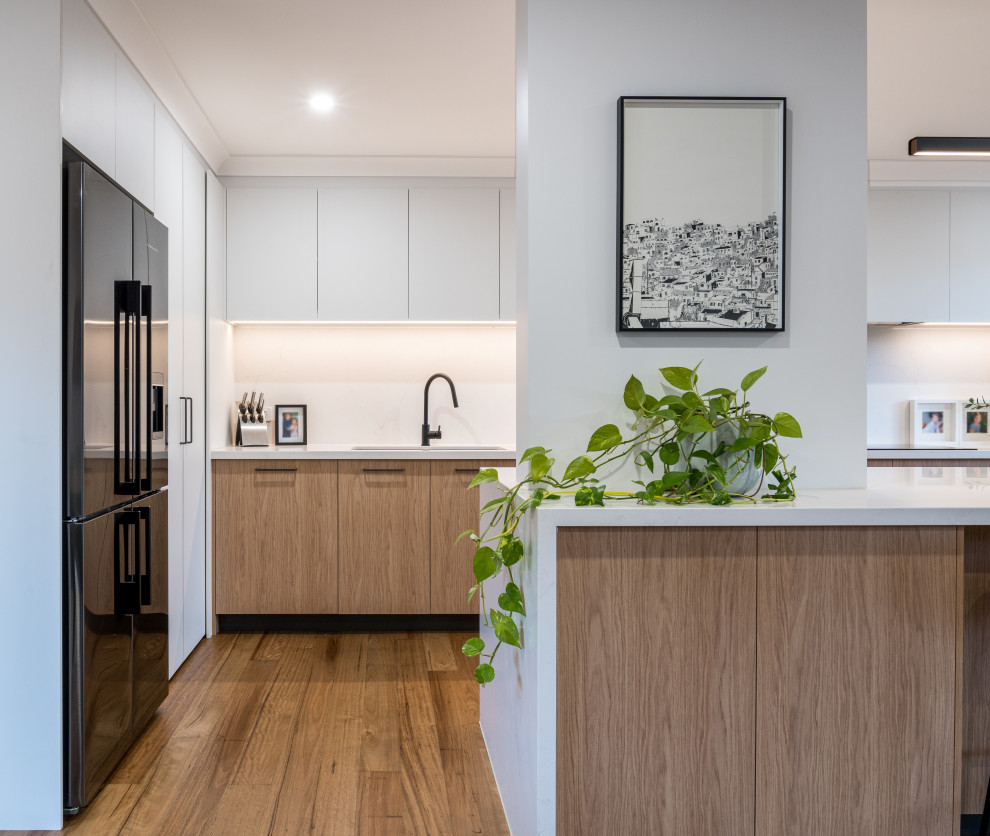 Inspiration for a mid-sized scandinavian l-shaped eat-in kitchen in Melbourne with an undermount sink, flat-panel cabinets, light wood cabinets, quartz benchtops, white splashback, engineered quartz splashback, black appliances, with island and white benchtop.