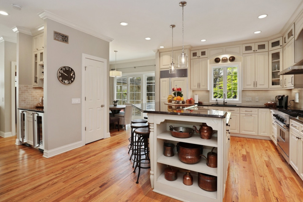 Inspiration for a large transitional l-shaped medium tone wood floor and brown floor eat-in kitchen remodel in Chicago with an undermount sink, raised-panel cabinets, white cabinets, white backsplash, stone tile backsplash, stainless steel appliances, an island and black countertops