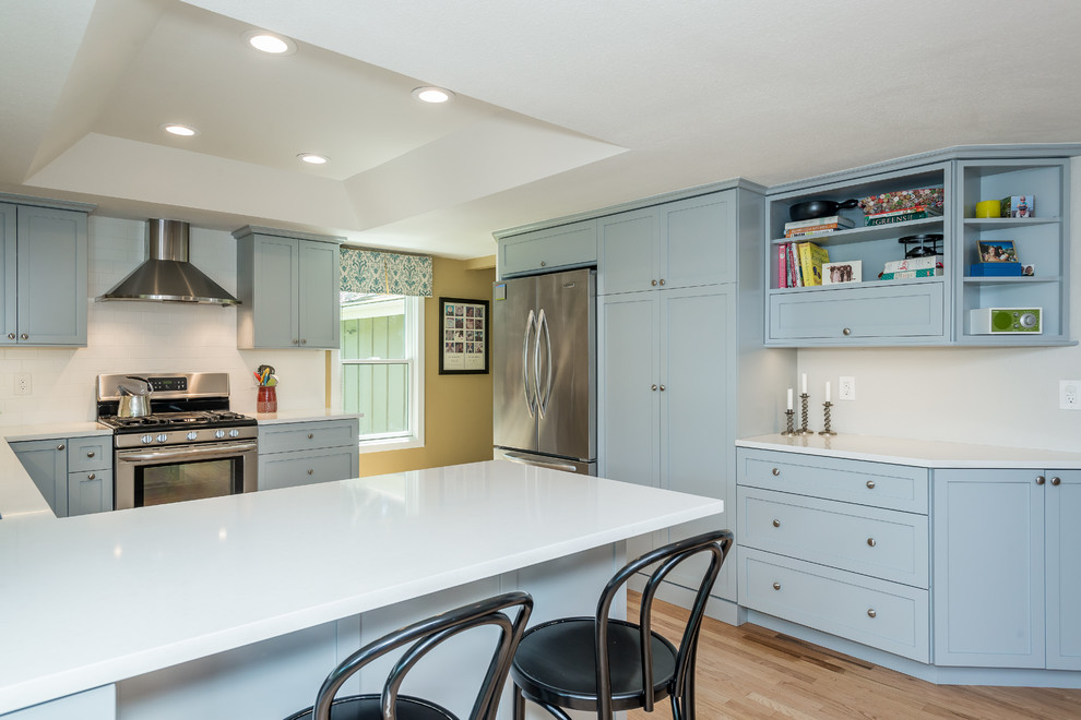 This is an example of a mid-sized transitional u-shaped eat-in kitchen in Denver with an undermount sink, shaker cabinets, grey cabinets, quartz benchtops, subway tile splashback, stainless steel appliances, light hardwood floors, a peninsula and white splashback.