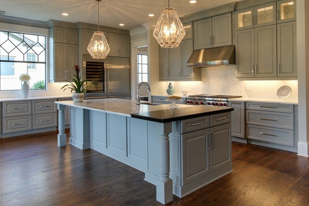 Inspiration for a large transitional l-shaped medium tone wood floor and brown floor open concept kitchen remodel with a farmhouse sink, raised-panel cabinets, green cabinets, marble countertops, white backsplash, stone tile backsplash, stainless steel appliances and an island