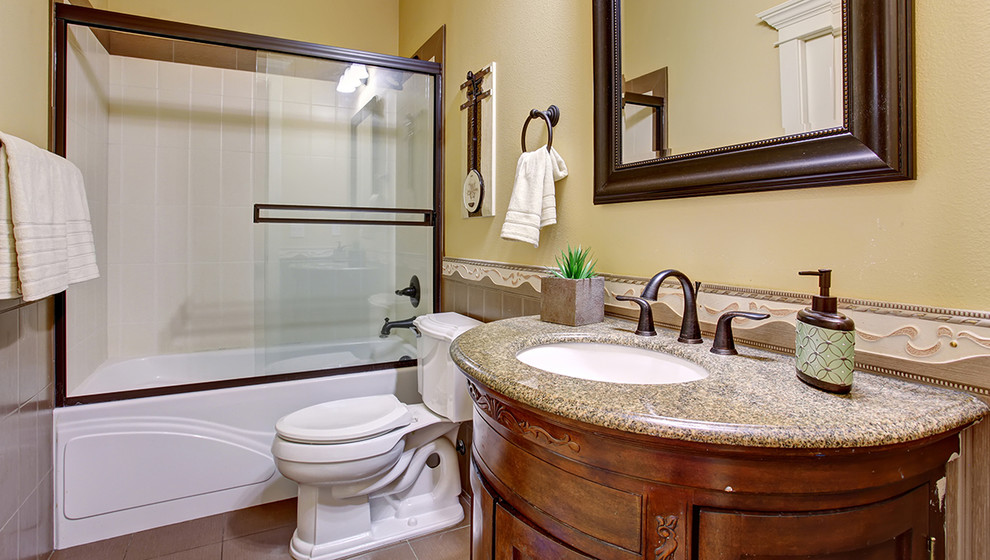 Mid-sized traditional 3/4 bathroom in Phoenix with shaker cabinets, dark wood cabinets, a shower/bathtub combo, a two-piece toilet, white tile, beige walls, ceramic floors, an undermount sink and granite benchtops.