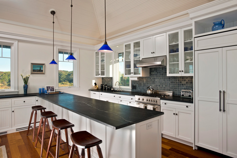 This is an example of a mid-sized beach style kitchen in New York with glass-front cabinets, soapstone benchtops, a single-bowl sink, multi-coloured splashback, mosaic tile splashback, panelled appliances, medium hardwood floors and a peninsula.