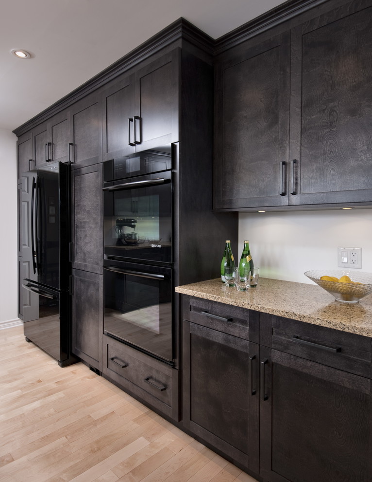 Example of a mid-sized transitional u-shaped light wood floor eat-in kitchen design with shaker cabinets, dark wood cabinets, quartz countertops, black appliances, a peninsula and beige countertops