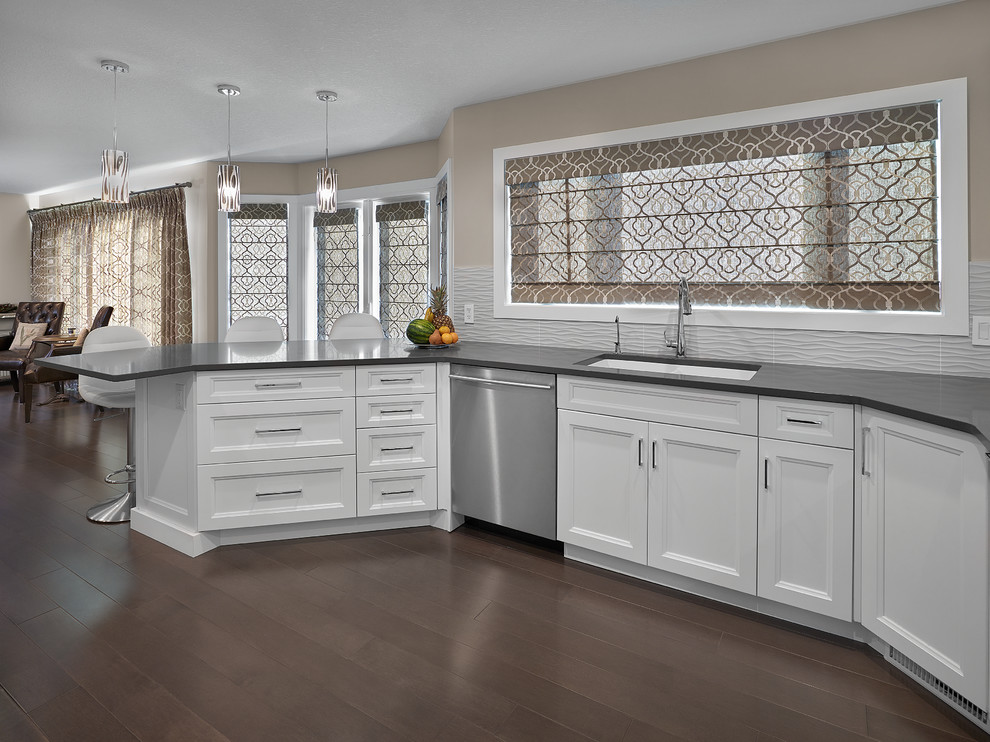 Eat-in kitchen - mid-sized transitional single-wall dark wood floor and brown floor eat-in kitchen idea in Edmonton with an undermount sink, recessed-panel cabinets, white cabinets, quartz countertops, white backsplash, stainless steel appliances and a peninsula