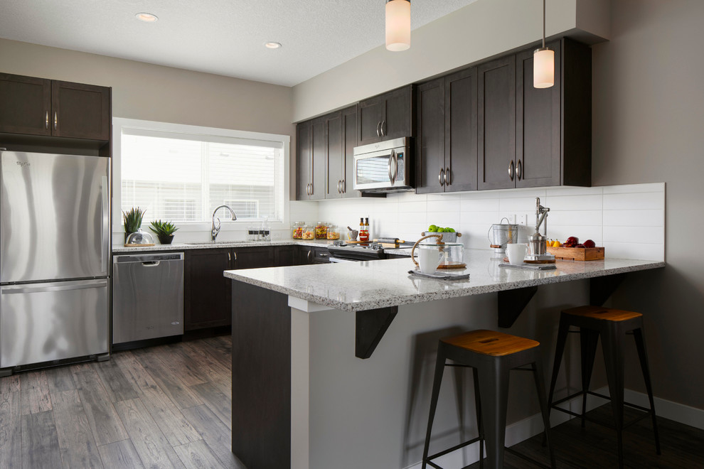 Mid-sized transitional u-shaped open plan kitchen in Calgary with an undermount sink, recessed-panel cabinets, medium wood cabinets, granite benchtops, white splashback, ceramic splashback, stainless steel appliances, light hardwood floors and a peninsula.