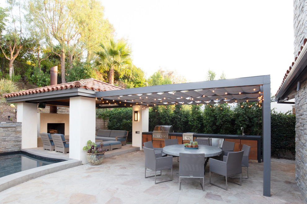 Mediterranean backyard patio in Orange County with an outdoor kitchen, natural stone pavers and a pergola.