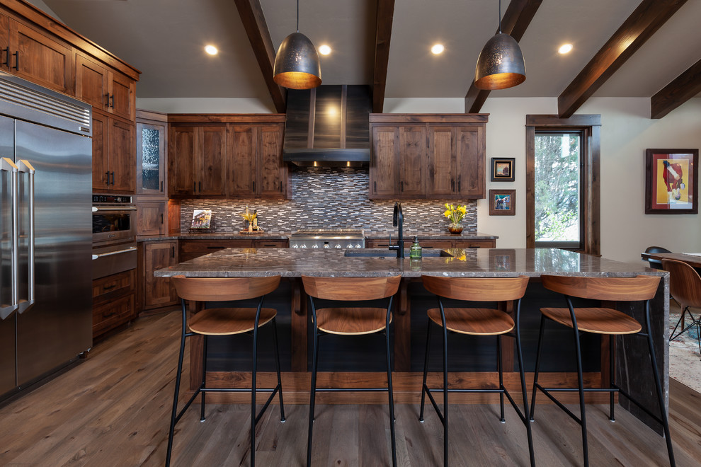 This is an example of a country l-shaped kitchen in Other with an undermount sink, shaker cabinets, dark wood cabinets, grey splashback, mosaic tile splashback, stainless steel appliances, medium hardwood floors, with island, brown floor and grey benchtop.