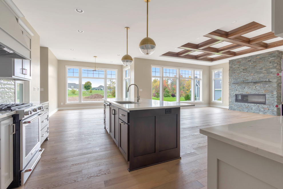 Transitional l-shaped medium tone wood floor, beige floor and coffered ceiling open concept kitchen photo in Milwaukee with an undermount sink, recessed-panel cabinets, white cabinets, quartz countertops, white backsplash, subway tile backsplash, stainless steel appliances, an island and white countertops