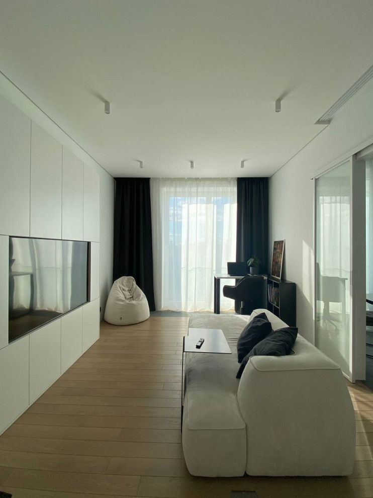 На фото: гостиная комната в белых тонах с отделкой деревом в современном стиле с белыми стенами, телевизором на стене, зоной отдыха, коричневым полом и красивыми шторами