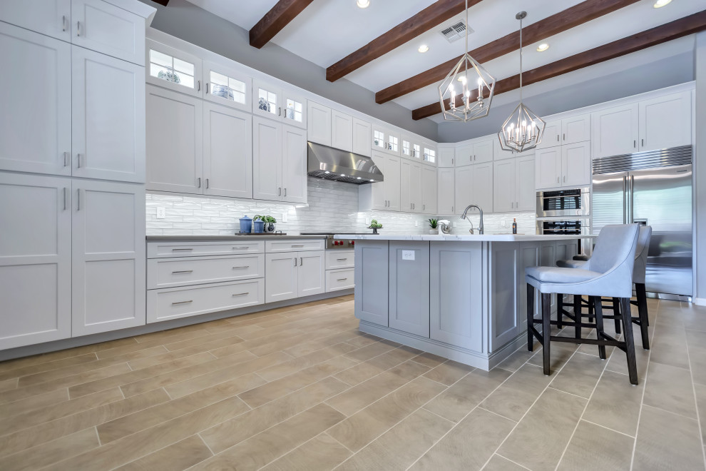 Eat-in kitchen - large transitional l-shaped porcelain tile and brown floor eat-in kitchen idea in Phoenix with a farmhouse sink, shaker cabinets, white cabinets, quartz countertops, white backsplash, subway tile backsplash, stainless steel appliances, an island and gray countertops