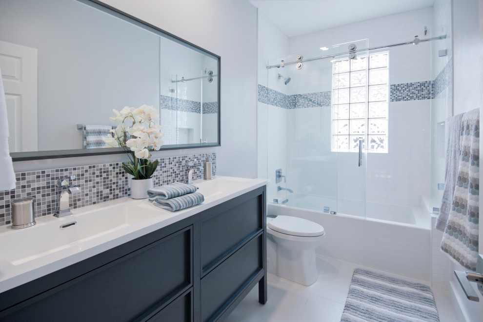 This is an example of a mid-sized contemporary kids bathroom in Miami with flat-panel cabinets, white cabinets, an alcove tub, a two-piece toilet, white tile, stone tile, grey walls, laminate floors, an undermount sink, engineered quartz benchtops, white floor, a sliding shower screen and white benchtops.