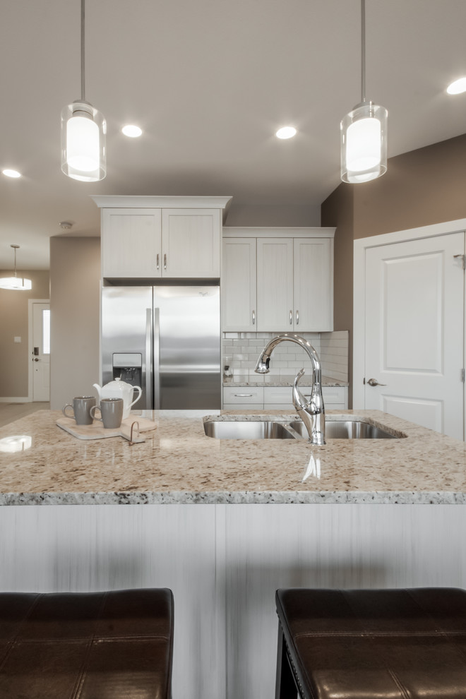 Design ideas for a mid-sized transitional l-shaped eat-in kitchen in Calgary with an undermount sink, shaker cabinets, white cabinets, granite benchtops, white splashback, subway tile splashback, stainless steel appliances, laminate floors and with island.