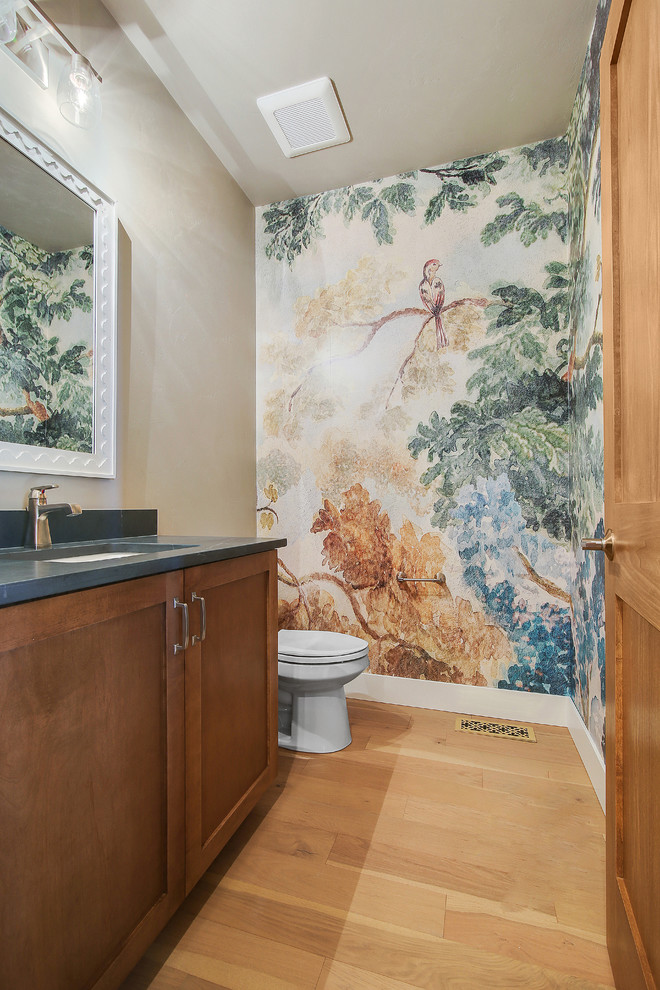 Eclectic powder room in Other with shaker cabinets, brown cabinets, a two-piece toilet, light hardwood floors, an undermount sink, soapstone benchtops and black benchtops.