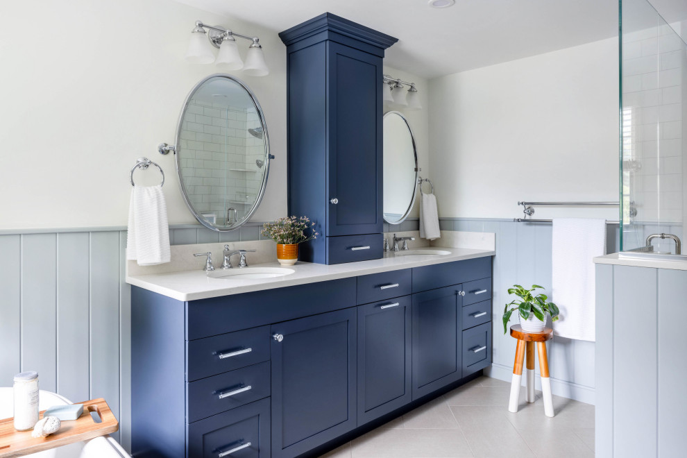 This is an example of a country master bathroom in Boston with shaker cabinets, blue cabinets, a freestanding tub, a corner shower, a two-piece toilet, white tile, ceramic tile, white walls, porcelain floors, an undermount sink, engineered quartz benchtops, beige floor, a hinged shower door, beige benchtops, a shower seat, a double vanity and a built-in vanity.