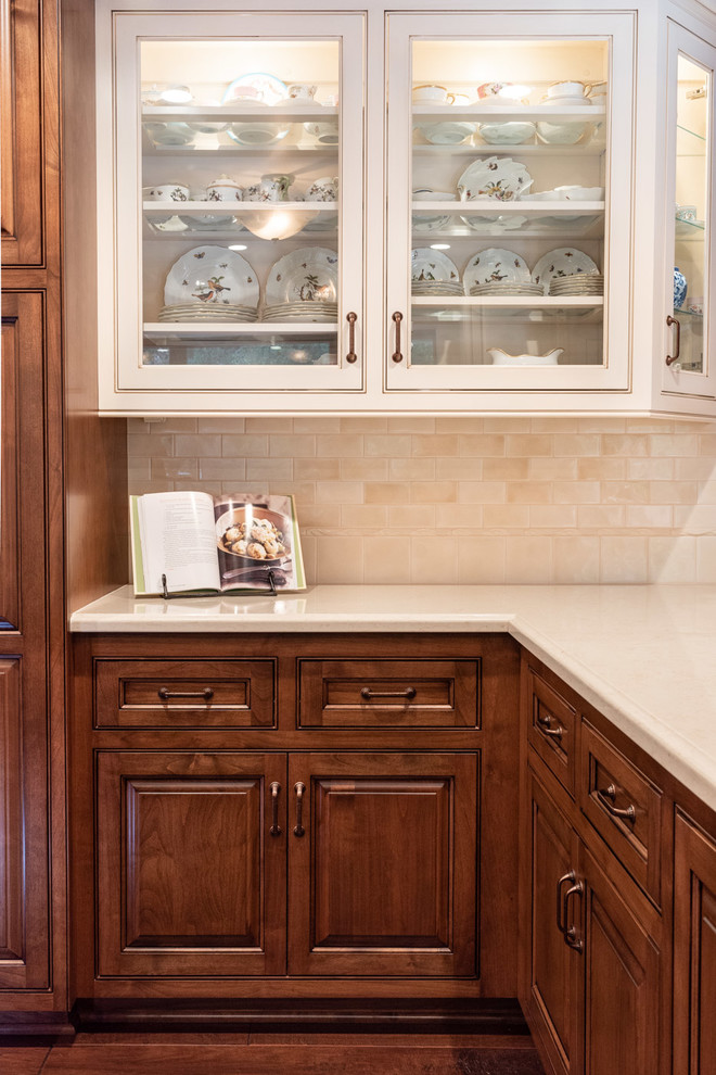 This is an example of a traditional u-shaped eat-in kitchen in San Luis Obispo with a drop-in sink, raised-panel cabinets, medium wood cabinets, quartz benchtops, beige splashback, porcelain splashback, panelled appliances, dark hardwood floors, with island, brown floor and white benchtop.