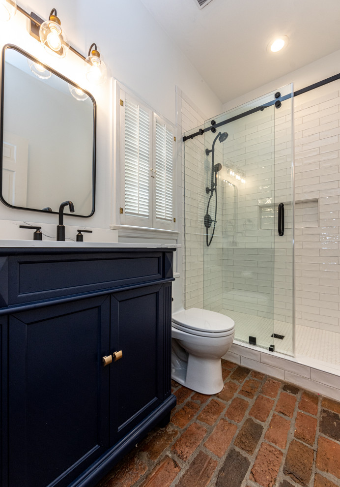 Свежая идея для дизайна: ванная комната среднего размера в стиле кантри с фасадами в стиле шейкер, синими фасадами, душем в нише, унитазом-моноблоком, белой плиткой, керамической плиткой, белыми стенами, кирпичным полом, душевой кабиной, врезной раковиной, столешницей из искусственного кварца, красным полом, душем с раздвижными дверями, белой столешницей, нишей, тумбой под одну раковину и напольной тумбой - отличное фото интерьера