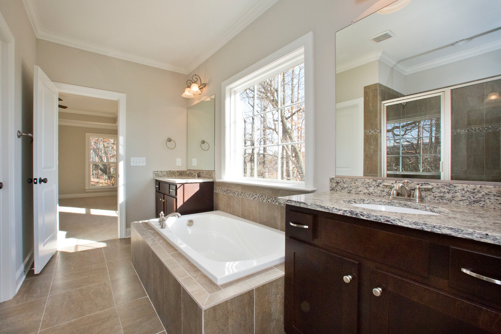 This is an example of a large transitional master bathroom in Raleigh with shaker cabinets, dark wood cabinets, a drop-in tub, a corner shower, beige walls, an undermount sink, beige floor and a hinged shower door.